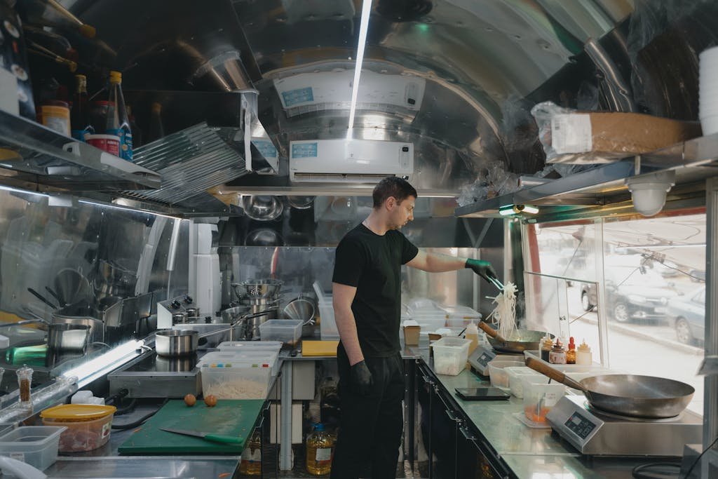 A man preparing food inside a stainless steel interior food truck kitchen.