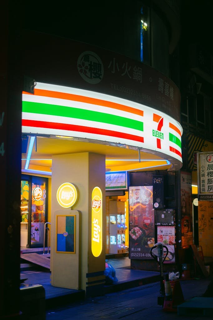 Colorful 7-Eleven convenience store illuminated in an urban area during night time, offering a lively city vibe.